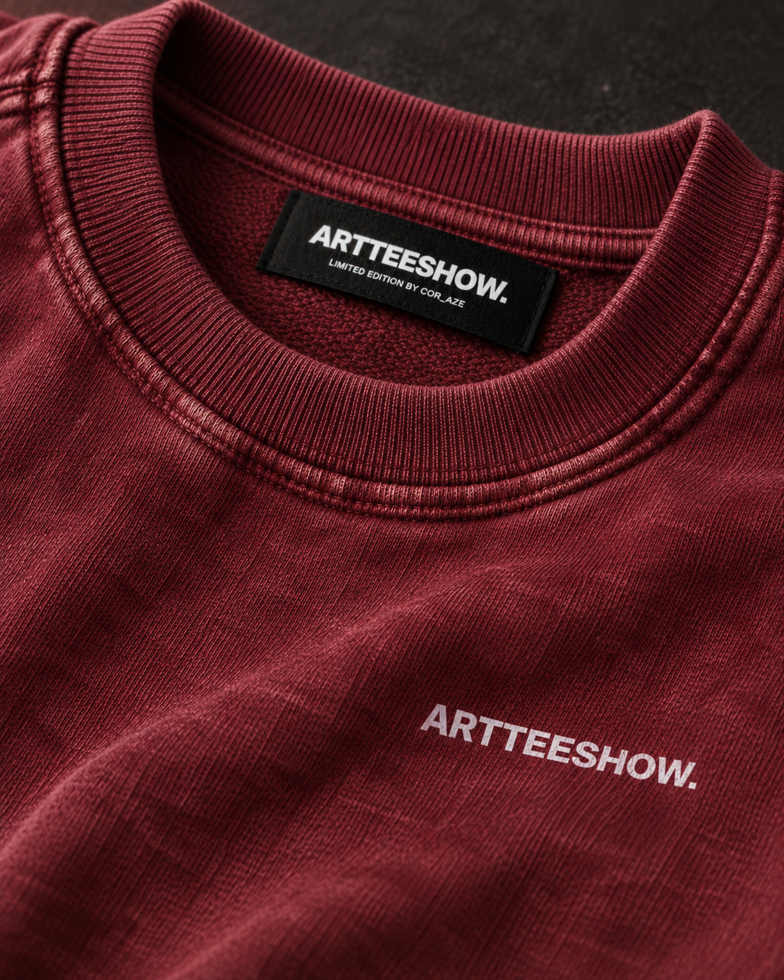 Close-up of a crewneck sweatshirt in a washed burgundy color, featuring the brand name 'ARTTEESHOW.' printed in white on the chest and a black neck label.