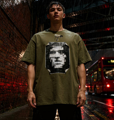 Model wearing a Khaki t-shirt with a graphic design by Ghost.Prompt in a rain-soaked urban London setting